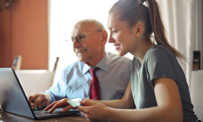 Young Woman Helping Senior To Transfer Money from Checking Account to Prepaid Card Online Concept