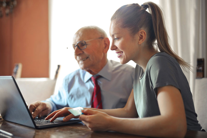 Young Woman Helping Senior To Transfer Money from Checking Account to Prepaid Card Online Concept