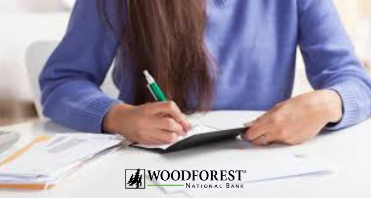 Person writing on a document at a desk with Woodforest National Bank logo indicating financial services like cashing third-party checks.